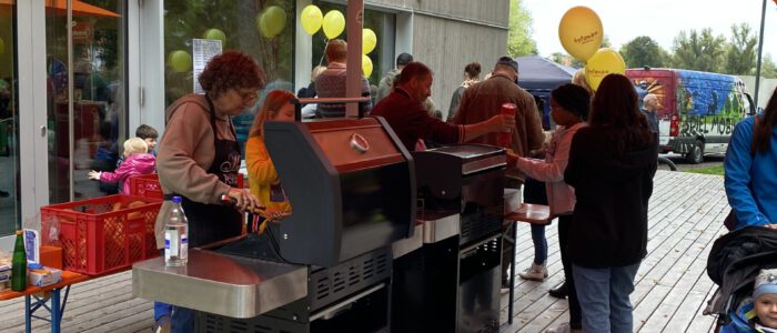 Bild des Kinder- und Familienfestes, auf dem Mitarbeitende Würstchen grillen und diese an Besucher*innen aushändigen