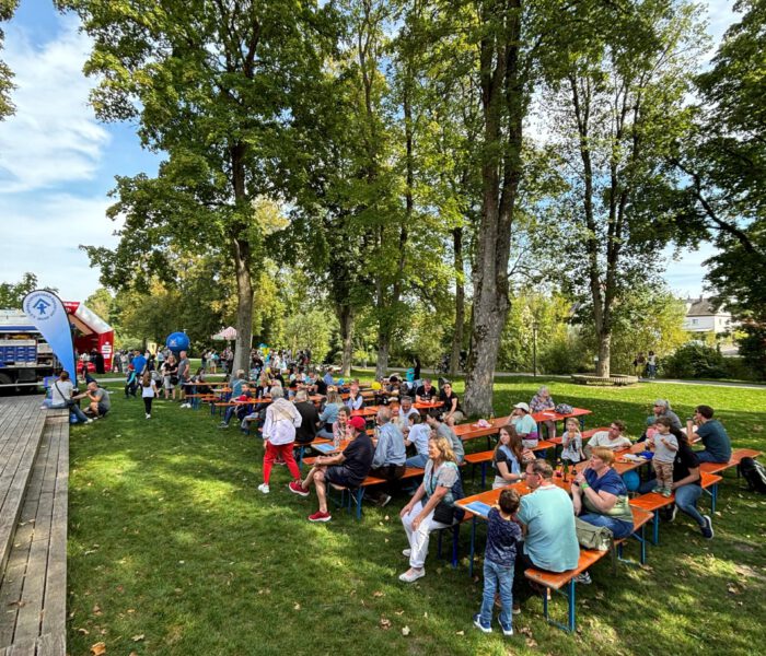 Bilder des Gartens des Jugendhauses am Kinder- und Familienfest 2024, Besucher*innen sitzen auf Bierbänken und bestaunen da Bühnenprogramm