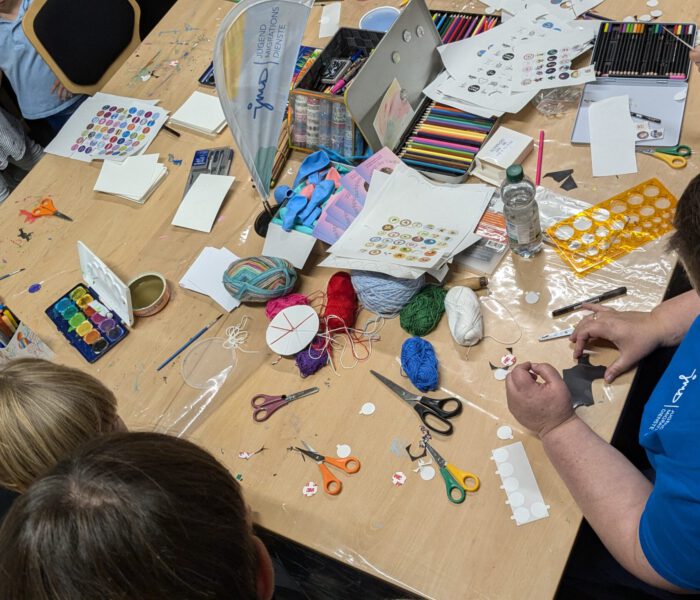 Bild eines Bastelangebotes beim Kinder- und Familienfest 2024, Kinder sitzen am Tisvchen und malen mit Wasserfarben